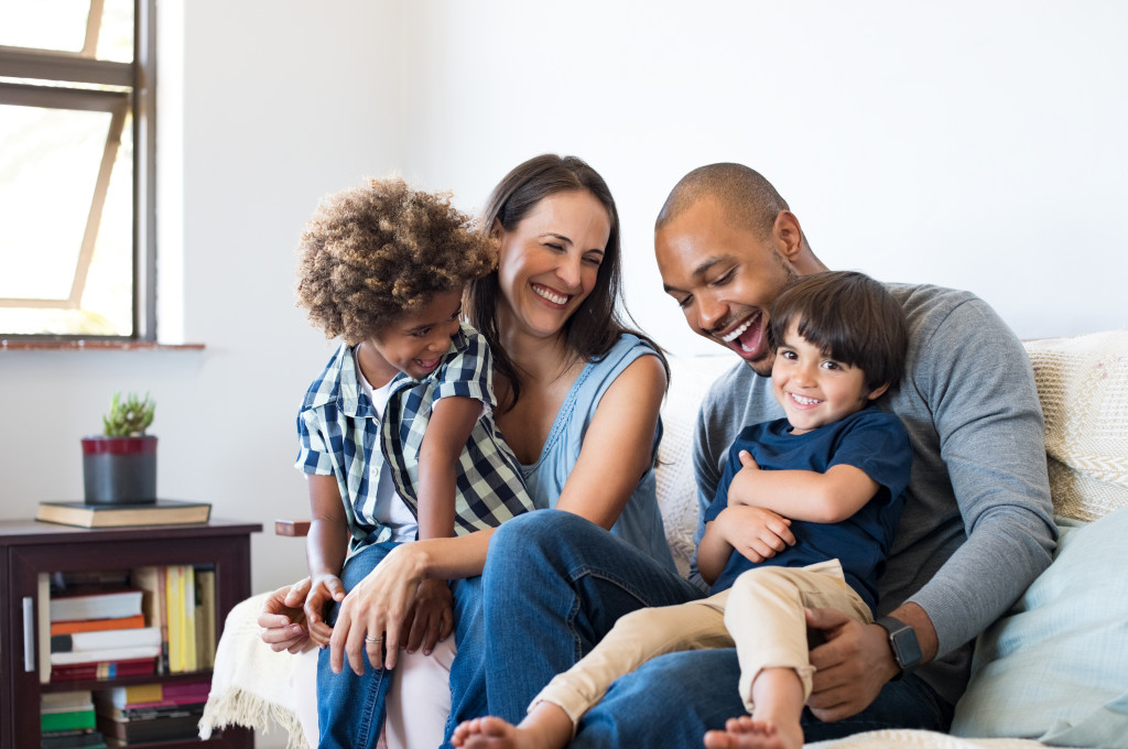 happy multiracial family at home sitting in sofa with two kids